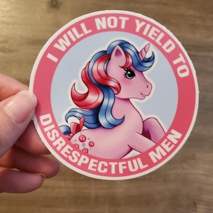 Puede incluir: Una pegatina redonda con borde rosa y el texto "I WILL NOT YIELD TO DISRESPECTFUL MEN". Presenta un pony rosa con pelo azul y rojo, sobre un fondo azul claro. El diseño recuerda a una caricatura.