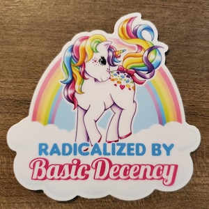 May include: A sticker showing a white unicorn with a rainbow mane and tail, set against a rainbow. The text "RADICALIZED BY Basic Decency" is below the unicorn in blue and pink.