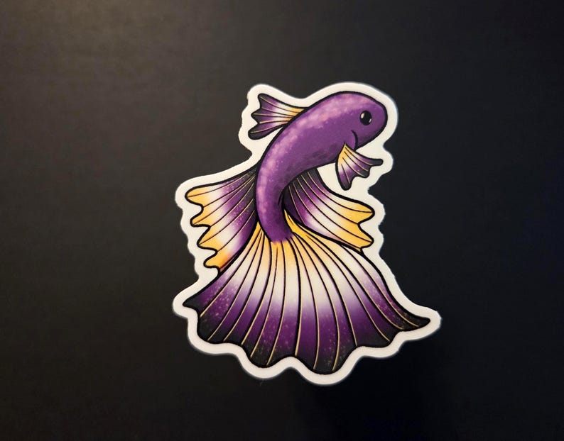 Op de afbeelding: Een sticker met een gestileerde paarse en gele betta-vis met een witte rand. De vis heeft gedetailleerde vinnen en een lachend gezicht. De sticker staat op een zwarte achtergrond.