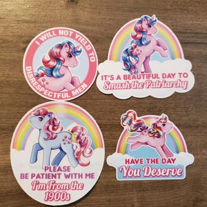 May include: Four vinyl stickers featuring cartoon ponies with rainbow backgrounds. One circular sticker reads I WILL NOT YIELD TO DISRESPECTFUL MEN. Another reads IT'S A BEAUTIFUL DAY TO Smash the Patriarchy. A third says PLEASE BE PATIENT WITH ME I'm From the 1900s. The last reads HAVE THE DAY You Deserve.