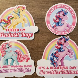 May include: Four vinyl stickers featuring cartoon ponies with rainbow motifs and text. One reads FUELED BY Feminist Rage, another I WILL NOT YIELD TO DISRESPECTFUL MEN, the third GIRLS JUST WANNA HAVE Fundamental Rights, and the last IT'S A BEAUTIFUL DAY TO Smash the Patriarchy.
