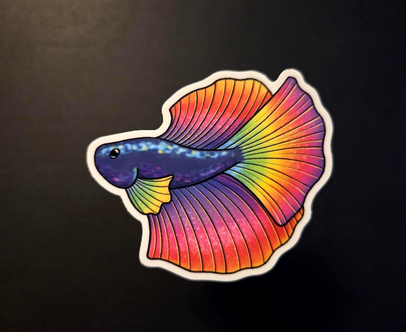 Op de afbeelding: Een kleurrijke sticker met een gestileerde vis met een levendige regenboogkleurige staart en vinnen. De vis heeft een donkerblauwe body met een witte omtrek, tegen een donkere achtergrond. De sticker is ontworpen in een cartoonachtige stijl.