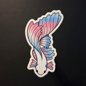 Op de afbeelding: Een sticker met een gestileerde betta-vis met een wit lichaam en roze en blauwe vinnen. De vis is afgebeeld in een sierlijke, gebogen pose, met de vinnen uitwaaierend. De sticker heeft een witte rand.
