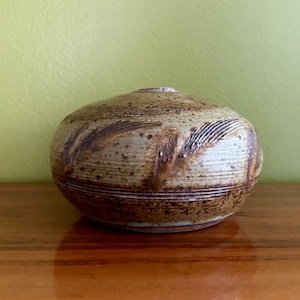 May include: A small, round, brown and white ceramic vase with a textured surface and a simple design.