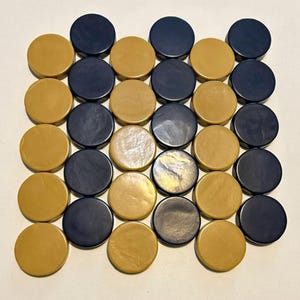 May include: A collection of thirty-two round game pieces, alternating between a mustard yellow and a deep navy blue. The pieces are arranged in a grid pattern, suggesting a board game.