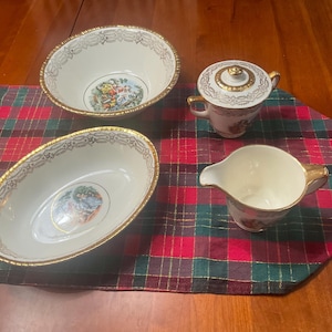 Puede incluir: Un juego de té vintage color crema con ribete dorado, que incluye dos cuencos ovalados, una azucarera con tapa y una jarra de crema. Cada pieza presenta una ilustración colorida y detallada.