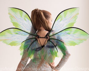May include: A woman wearing a sheer bodysuit with a white lace pattern and a pair of white high heels. She is wearing a pair of large, green and blue butterfly wings.