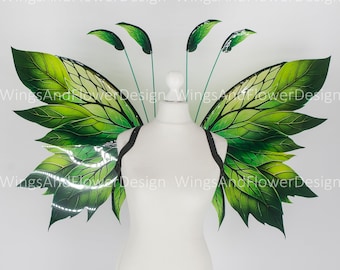 Op de afbeelding: Een paar groene feeënvleugels met een bladontwerp. De vleugels zijn bevestigd aan een wit mannequin torso.