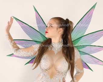 May include: A woman wearing a sparkly, sheer bodysuit with a pair of large, iridescent butterfly wings. The wings are green, purple, and pink with a delicate vein pattern.