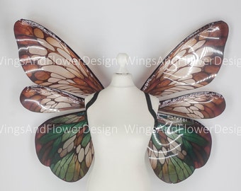 May include: A pair of large, iridescent butterfly wings with brown, green, and white patterns. The wings are made of a translucent material and have a delicate, ethereal look.