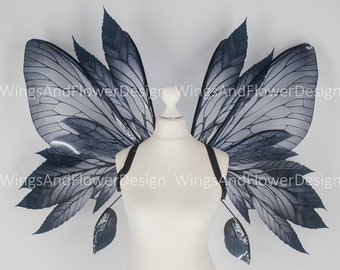 May include: A pair of black and silver fairy wings with a leaf design. The wings are attached to a white mannequin.