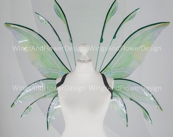 May include: A pair of green and white fairy wings with a clear iridescent finish. The wings are attached to a black harness and are displayed on a white mannequin.