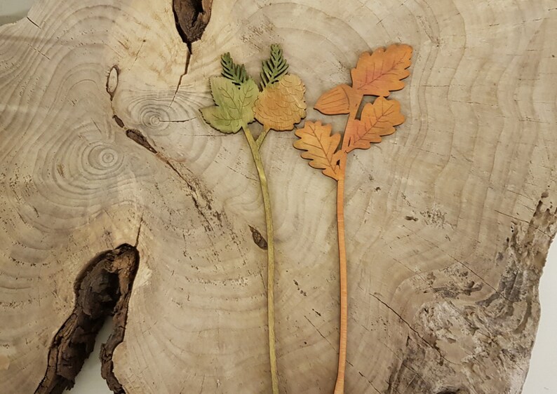 May include: Two wooden floral stems with leaves and flowers. The stem on the left has green leaves and orange flowers. The stem on the right has orange leaves and a brown acorn.