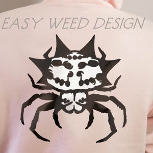 May include: A pink hoodie with a black spider design on the back. The spider has a skull-like face and a spiky body. The text "EASY WEED DESIGN" is printed above the spider.