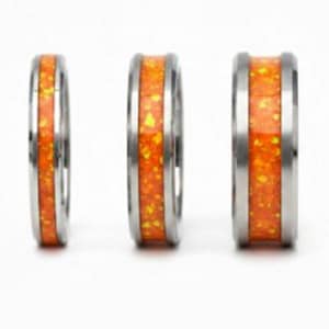 Könnte beinhalten: Drei silberne Ringe mit einem leuchtend orangefarbenen Mittelband. Die Ringe haben eine polierte, metallische Oberfläche und eine helle, gesprenkelte orangefarbene Einlage. Die Ringe werden vor weißem Hintergrund gezeigt.