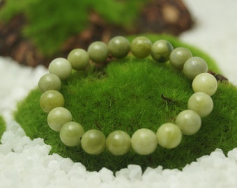May include: A green jade bead bracelet on a bed of green moss. The bracelet is made of smooth, round beads.