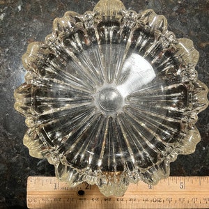 Puede incluir: Un cenicero de vidrio transparente con un borde festoneado y un diseño de rayos de sol. El cenicero tiene un diámetro de aproximadamente 12,7 cm.