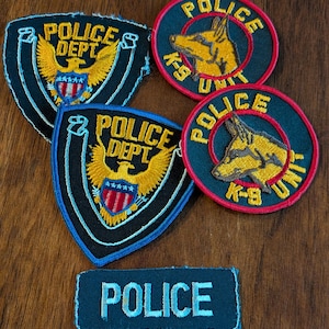 Puede incluir: Una colección de parches de policía, que incluye dos parches en forma de escudo con un emblema de águila y el texto "POLICE DEPT". Dos parches circulares presentan un perro y el texto "POLICE K-9 UNIT". Un parche rectangular dice "POLICE."