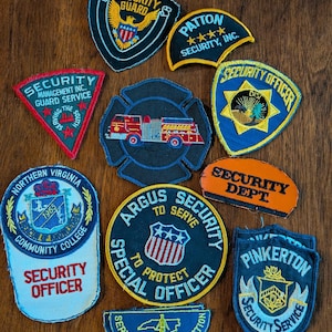 May include: A collection of embroidered security patches in various shapes and colors. The patches feature text such as "Security Guard," "Security Officer," and "Pinkerton." Some patches have emblems like an eagle, a fire truck, and a shield.