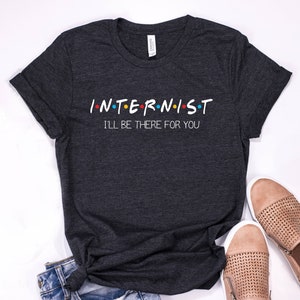May include: Dark gray t-shirt with the text "INTERNIST I'LL BE THERE FOR YOU" in white. The text is styled like the "Friends" logo.