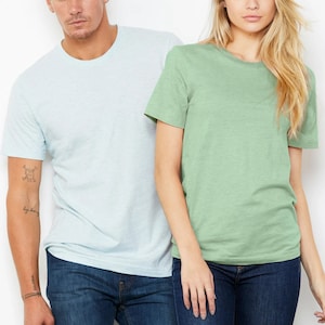 Puede incluir: Dos camisetas lisas, una azul claro y otra verde claro, son usadas por dos personas. Ambas camisetas son de manga corta y cuello redondo.