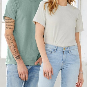 Puede incluir: Dos personas con camisetas lisas, una azul claro y otra beige claro. La persona que lleva la camiseta azul claro tiene un tatuaje en el brazo que dice "XII.XXIV.LXI".