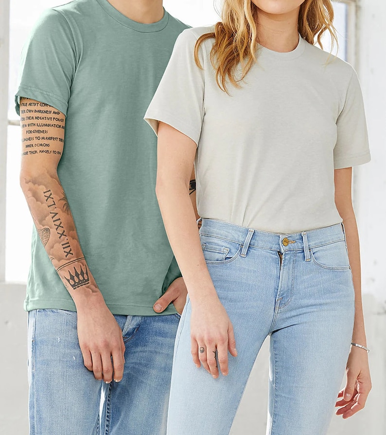 Puede incluir: Dos personas con camisetas lisas, una azul claro y otra beige claro. La persona que lleva la camiseta azul claro tiene un tatuaje en el brazo que dice "XII.XXIV.LXI".