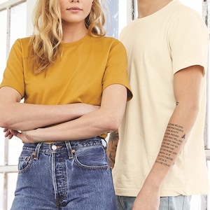 Puede incluir: Dos personas vistiendo camisetas. La persona de la izquierda lleva una camiseta amarilla mostaza y pantalones vaqueros azules. La persona de la derecha lleva una camiseta de color crema y pantalones vaqueros azules. La persona de la derecha tiene un tatuaje en el brazo que dice "El futuro pertenece a aquellos que creen en la belleza de sus sue&ntilde;os.  Todo aquel que quiera encender sus sue&ntilde;os puede llegar lejos.  Todo el mundo encuentra su propio c&oacute;digo.  Incluso si la vida te lanza una bola curva, siempre puedes vivir como si fueras a morir hoy."