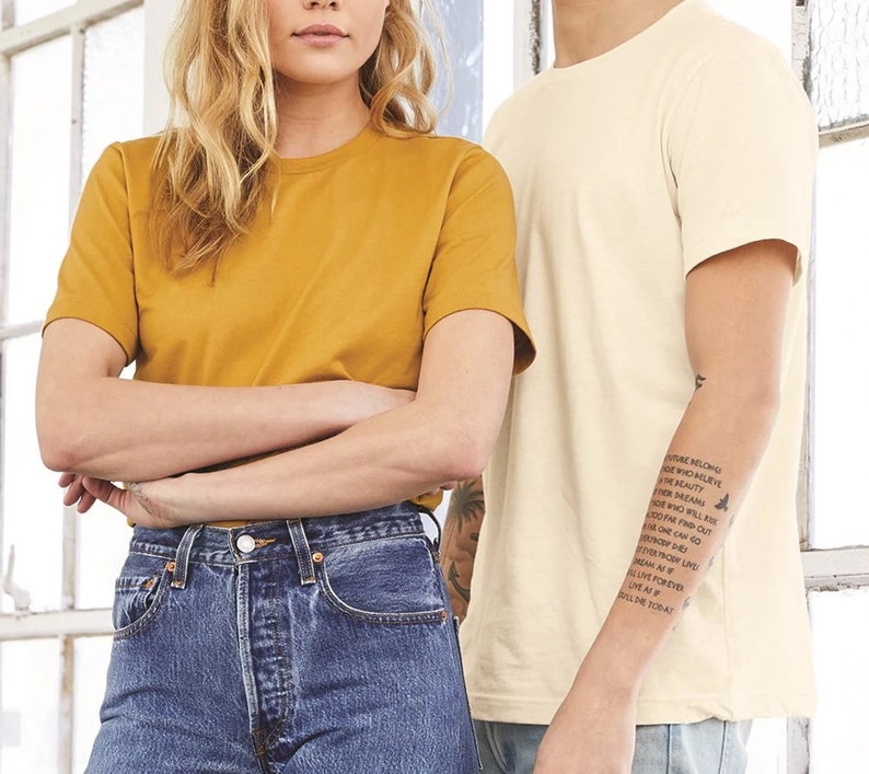 Puede incluir: Dos personas vistiendo camisetas. La persona de la izquierda lleva una camiseta amarilla mostaza y pantalones vaqueros azules. La persona de la derecha lleva una camiseta de color crema y pantalones vaqueros azules. La persona de la derecha tiene un tatuaje en el brazo que dice "El futuro pertenece a aquellos que creen en la belleza de sus sue&ntilde;os.  Todo aquel que quiera encender sus sue&ntilde;os puede llegar lejos.  Todo el mundo encuentra su propio c&oacute;digo.  Incluso si la vida te lanza una bola curva, siempre puedes vivir como si fueras a morir hoy."