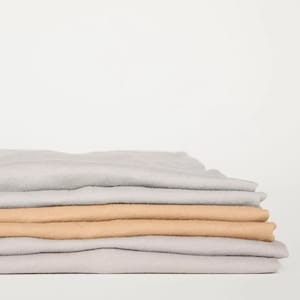 Puede incluir: Una pila de camisetas dobladas en gris claro y beige.
