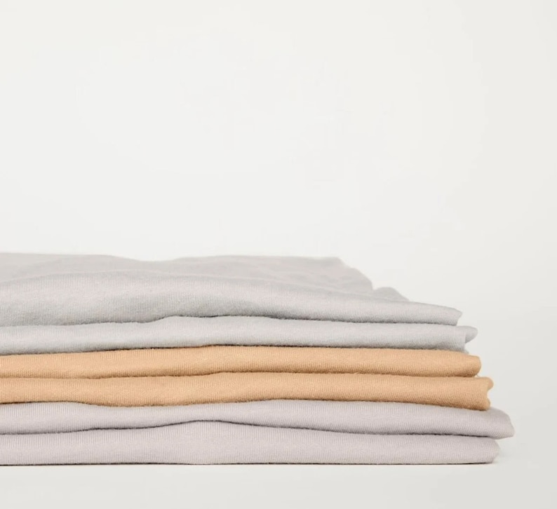 Puede incluir: Una pila de camisetas dobladas en gris claro y beige.