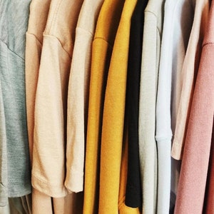 Puede incluir: Una colecci&oacute;n de camisetas dobladas en varios colores, incluyendo azul claro, beige, amarillo y rosa.