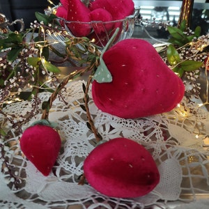 Könnte beinhalten: Ein weißer Spitzenuntersetzer mit einer Lichterkette auf einem silbernen Tablett.  Auf dem Untersetzer liegen mehrere rote Samt-Erdbeeren. Im Hintergrund ist ein silberner Krug zu sehen.