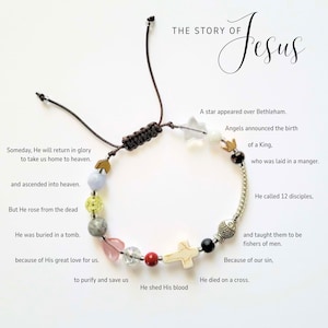 Pu&ograve; includere: Un braccialetto di perline con un cordoncino marrone e varie perline colorate, tra cui una croce, una stella e perline a forma di cuore. Il testo "THE STORY OF Jesus" &egrave; sopra il braccialetto, con testo aggiuntivo.