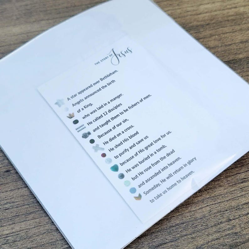 Pu&ograve; includere: Una carta bianca con il testo "THE STORY OF Jesus" e una poesia sulla vita di Ges&ugrave;. La carta &egrave; sopra una carta bianca pi&ugrave; grande, con una superficie di legno sullo sfondo.