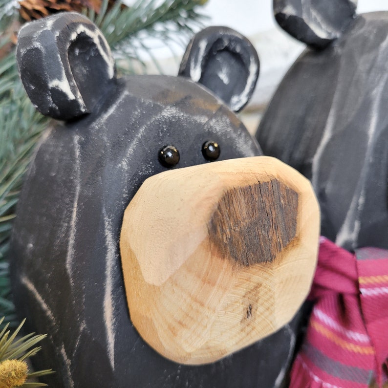 May include: Close-up of a black wooden bear figurine with a light brown wooden nose. The bear has black eyes and white accents on the ears. A second bear is partially visible in the background.