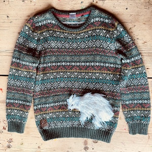May include: A green, red and white patterned jumper with a white fluffy pom-pom attached to the front.