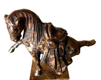 May include: A bronze sculpture of a horse with a saddle, standing on a square base. The horse is in a rearing pose, with its head turned to the side. The sculpture has a patina finish, giving it a weathered look.