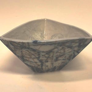 Puede incluir: Un cuenco de cerámica hecho a mano con una forma geométrica única. El cuenco presenta un interior blanco y un patrón abstracto azul y marrón en el exterior. El cuenco mide aproximadamente 15 cm de ancho y 7,6 cm de alto.