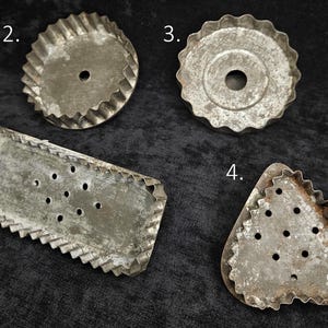 May include: Four vintage metal cookie cutters in various shapes. Includes a rectangle with holes, two scalloped circles, and a triangle with holes. The cutters have a rustic, aged appearance.