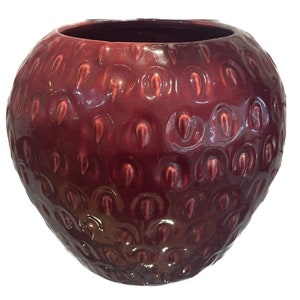 Könnte beinhalten: Eine runde, burgunderfarbene Keramikvase mit strukturierter Oberfläche. Die Vase hat eine glänzende Oberfläche und eine weite Öffnung. Die Textur ähnelt einer Erdbeere. Die Vase ist ein dekorativer Gegenstand.