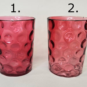 Könnte beinhalten: Zwei rubinrote Trinkgläser mit einem strukturierten, blasenartigen Muster. Die Gläser sind zylindrisch mit einem leicht ausgestellten Rand. Die Farbe ist durchgehend, mit einem dunkleren Farbton an der Basis und am Rand.