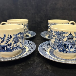 May include: Four matching teacups and saucers with a classic blue and white Willow pattern. The cups and saucers feature detailed scenes of pagodas, bridges, and birds. The cups have a curved handle and the saucers are round.