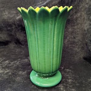 Può includere: Un vaso di ceramica verde con un design scanalato e un bordo giallo. Il vaso ha una base a piedistallo e una finitura craquelé. Il vaso è alto circa 20 cm.