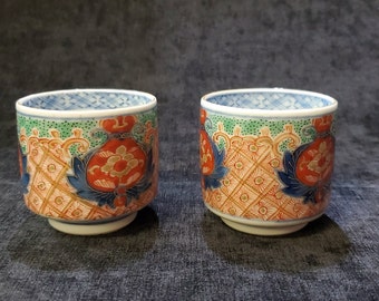 Puede incluir: Dos tazas de té de cerámica de estilo japonés. Las tazas presentan un diseño vibrante con patrones florales rojos, azules y verdes. Las tazas tienen forma redonda con una pequeña base con pie y un borde detallado.