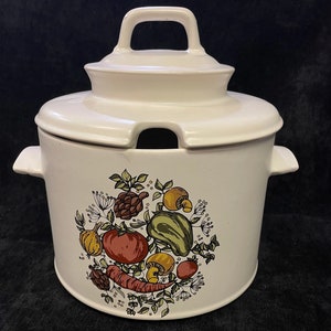 Op de afbeelding: Crèmekleurige keramische soepterrine met deksel en handvat. De terrine heeft een kleurrijke illustratie van groenten, waaronder tomaten, wortelen en champignons. Het deksel heeft een inkeping voor een lepel en een handvat.