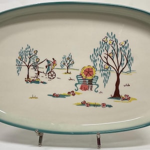 May include: A rectangular serving platter with a cream-colored surface and a teal border. The platter features a pastoral scene with trees, a bench, and figures, creating a vintage aesthetic. The design includes a horse-drawn carriage.