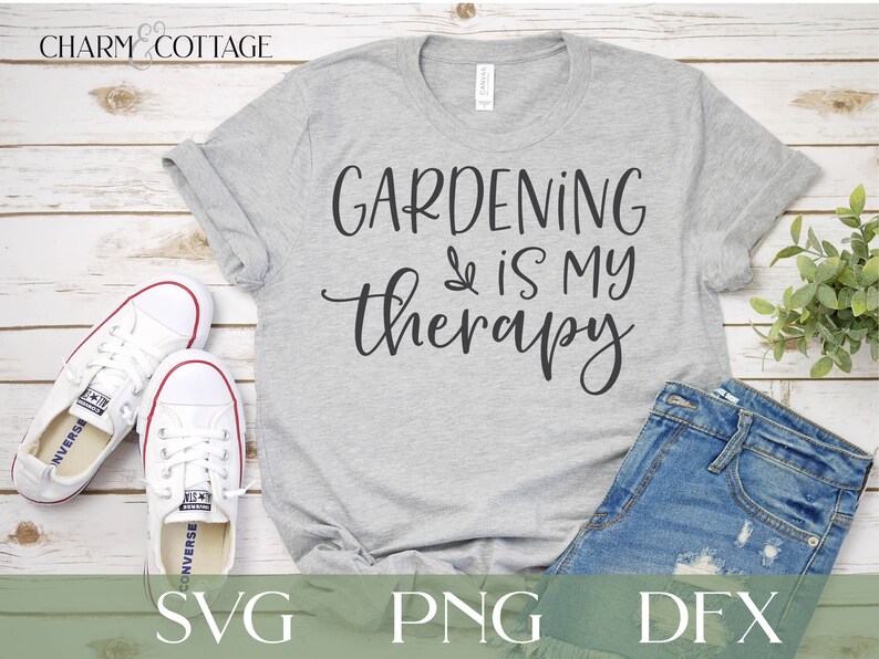 May include: A gray t-shirt with the text "GARDENING is my therapy" in black script font. The shirt is laid flat on a white wood background with a pair of white sneakers and a pair of blue jeans.