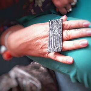 Peut inclure: Une bague noire avec une surface texturée, portée sur un doigt.