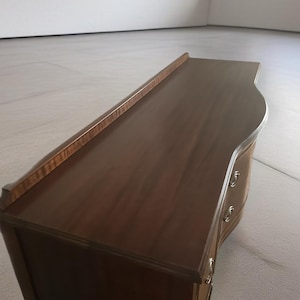 May include: A dark brown wooden dresser with two drawers and a curved front. The dresser has brass hardware and a smooth, polished finish.
